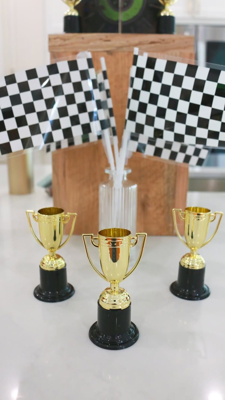Three gold trophies and checkered racing flags on a white table surface.