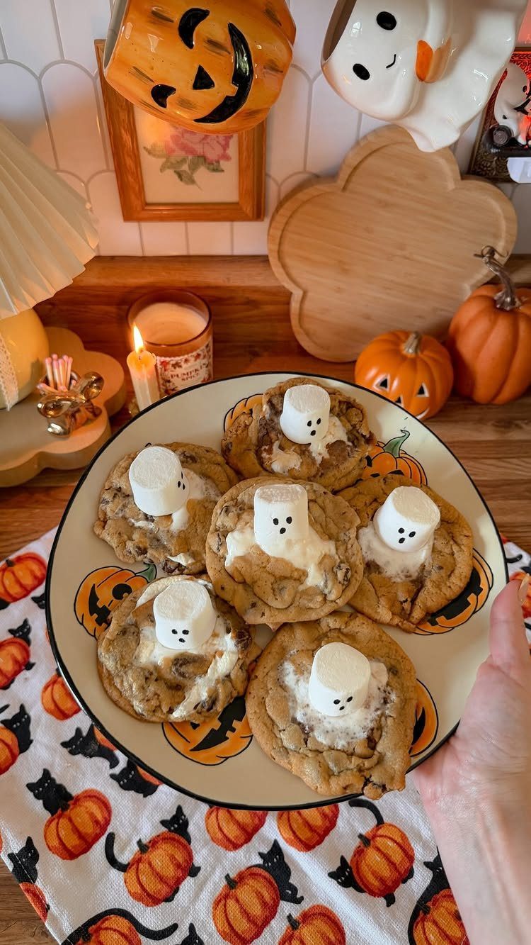 Ghost-themed chocolate chip cookies on a plate with Halloween decorations and pumpkins.