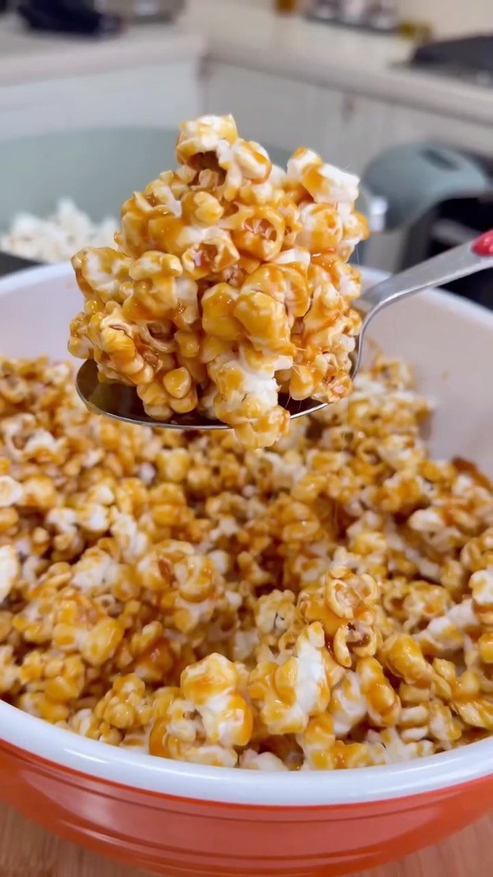 Caramel popcorn in a white and orange bowl being lifted by a spoon.