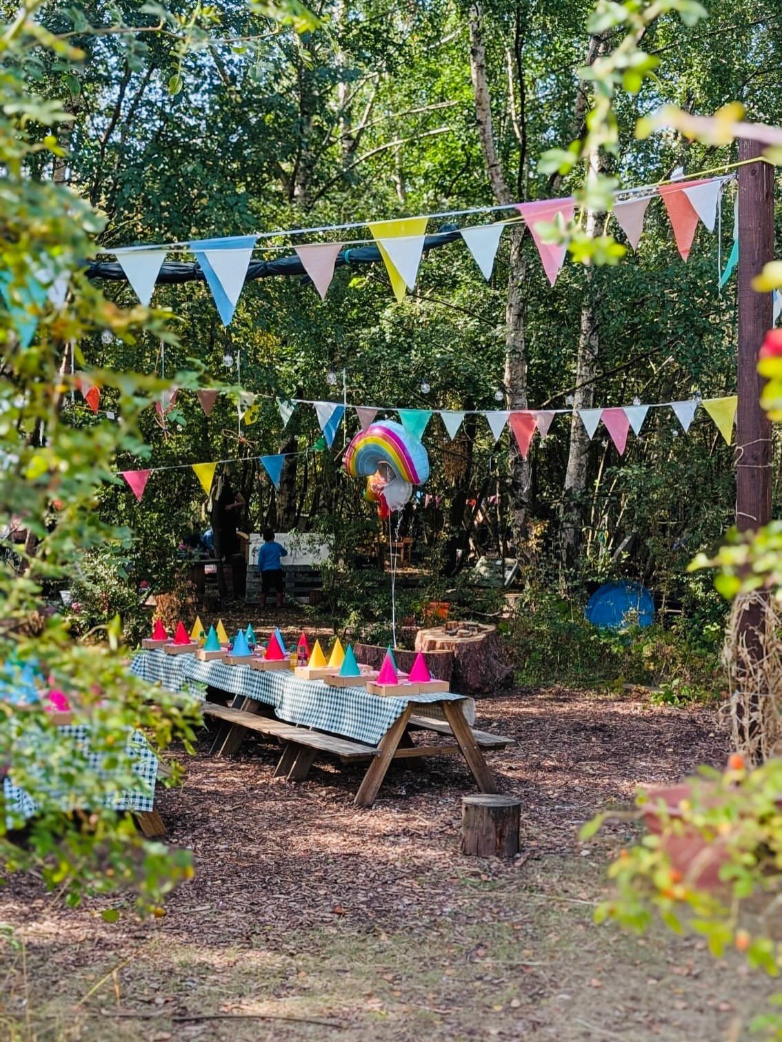 Picnic table with party hats and colorful bunting banners in a wooded setting