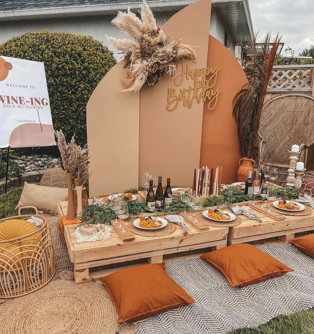 Outdoor birthday picnic with low pallet tables, orange cushions, and a beige backdrop.
