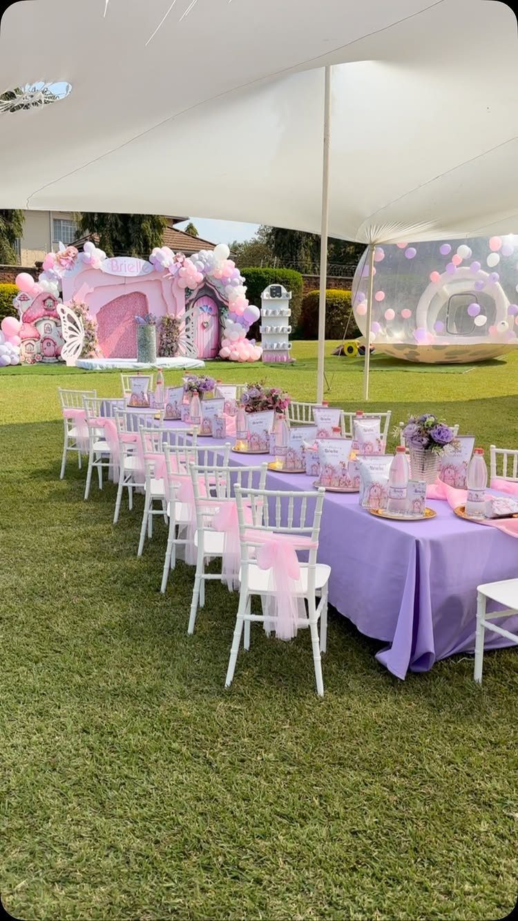 Purple party table and white chairs under a white tent on a lawn