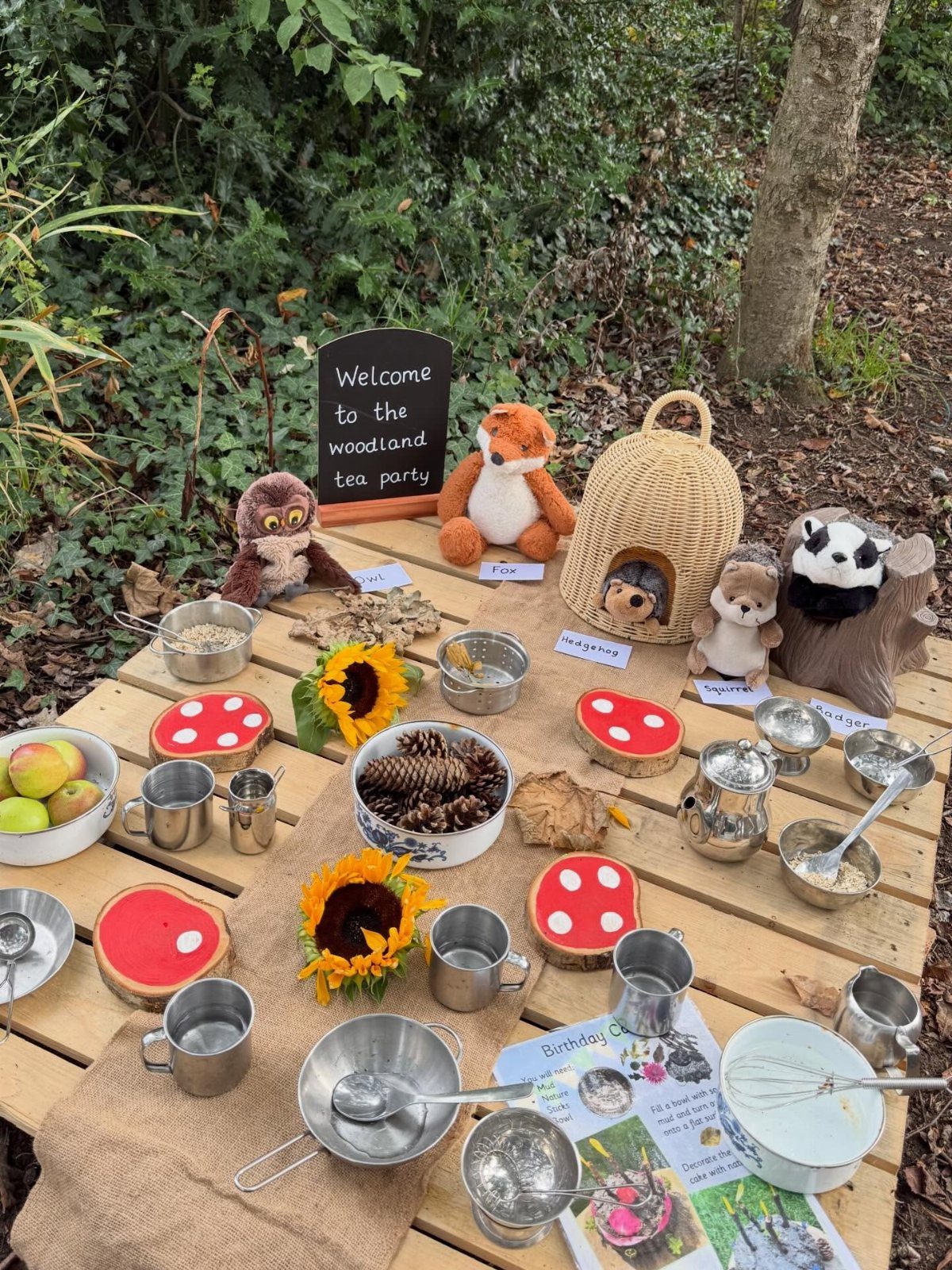 Woodland tea party setup on a pallet with stuffed animals and nature elements.
