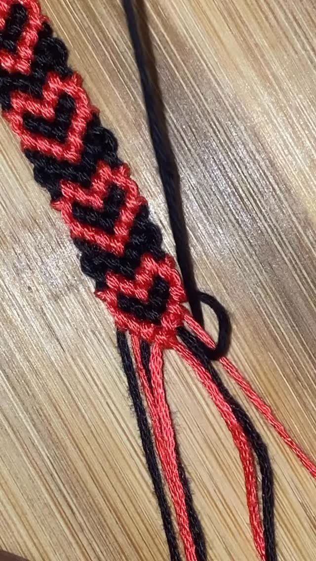 Woven friendship bracelet with red hearts on black thread on wooden surface