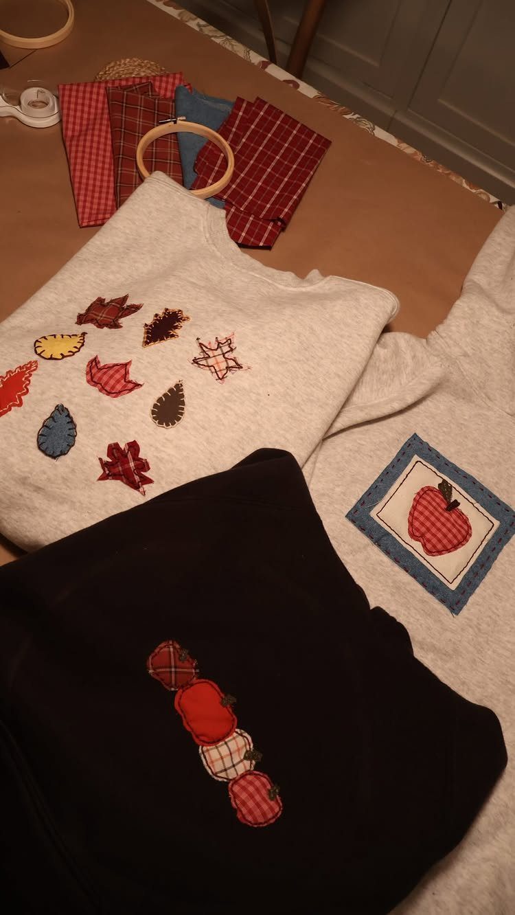 Embroidered sweatshirts with autumn leaves and apples next to sewing supplies