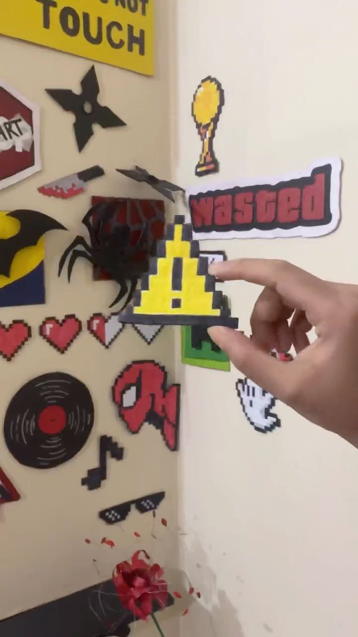 Hand holding a pixel-art bead warning sign against a wall of bead crafts.