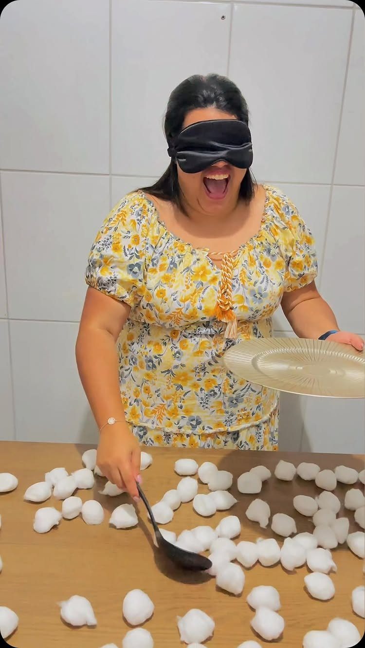 Blindfolded woman with a spoon and plate playing a game with cotton balls.