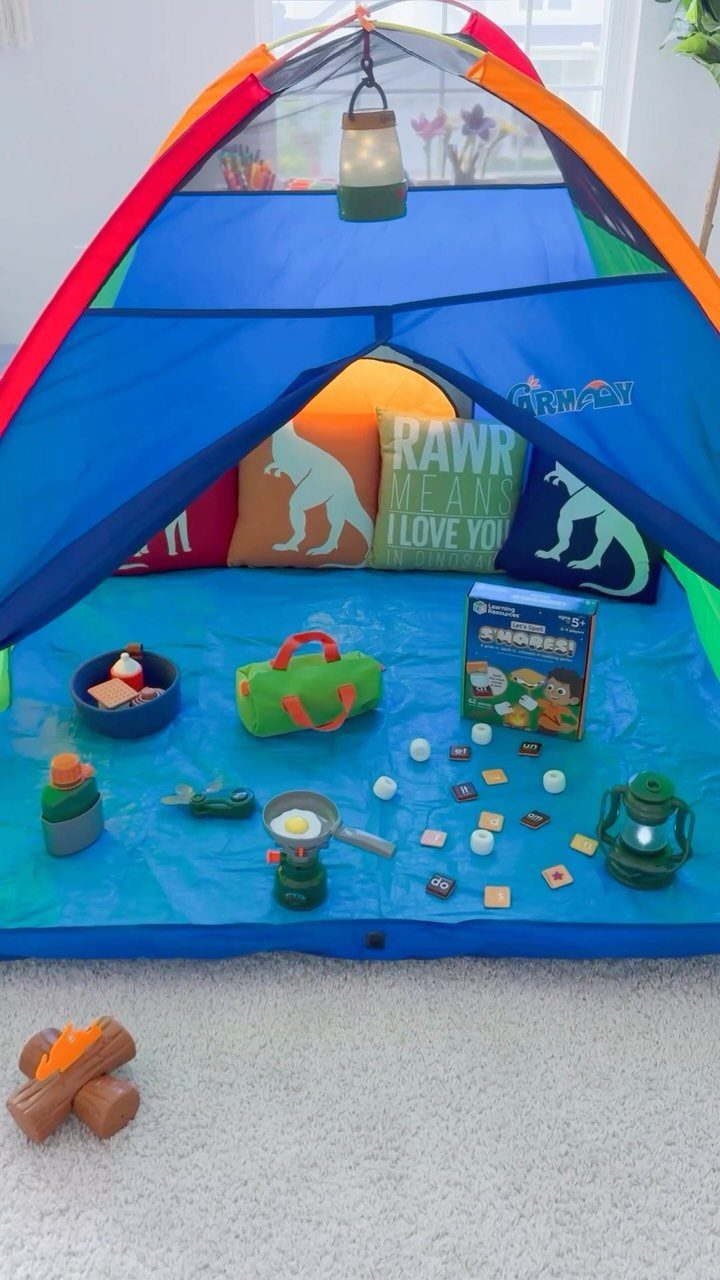 Colorful indoor play tent with dinosaur pillows and toy camping gear on a mat