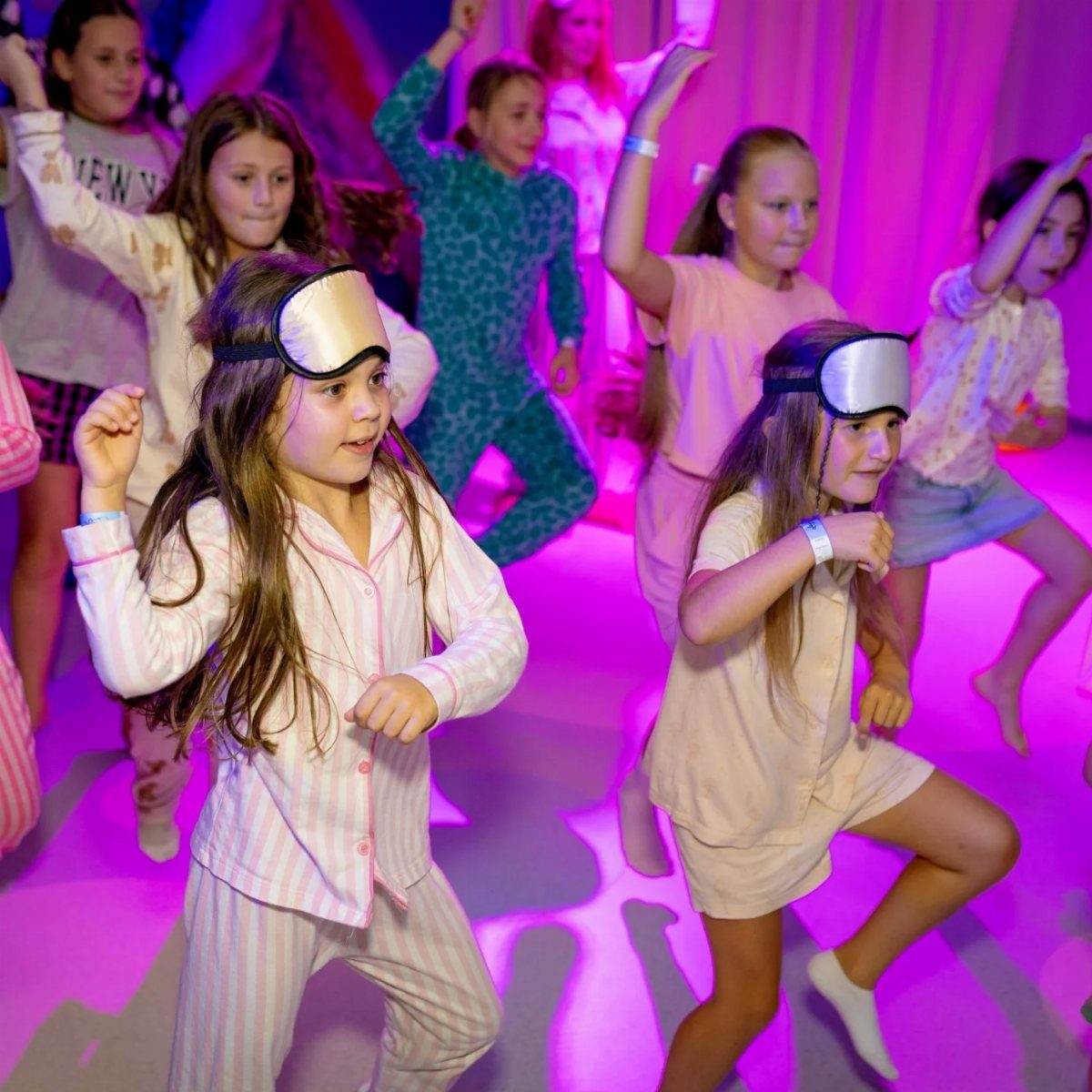 Young girls in pajamas and sleep masks dancing in a purple lit room.