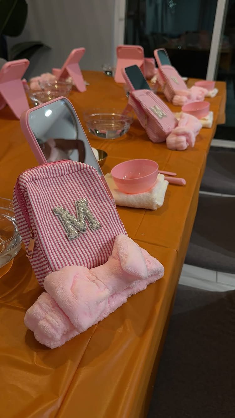 Pink spa kits with headbands, bowls, and mirrors arranged on an orange table.