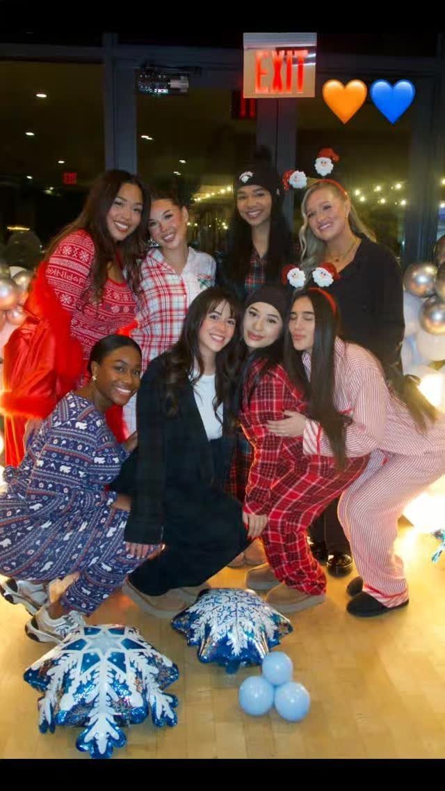 Group of women in pajamas posing with snowflake pillows and blue balloons indoors.