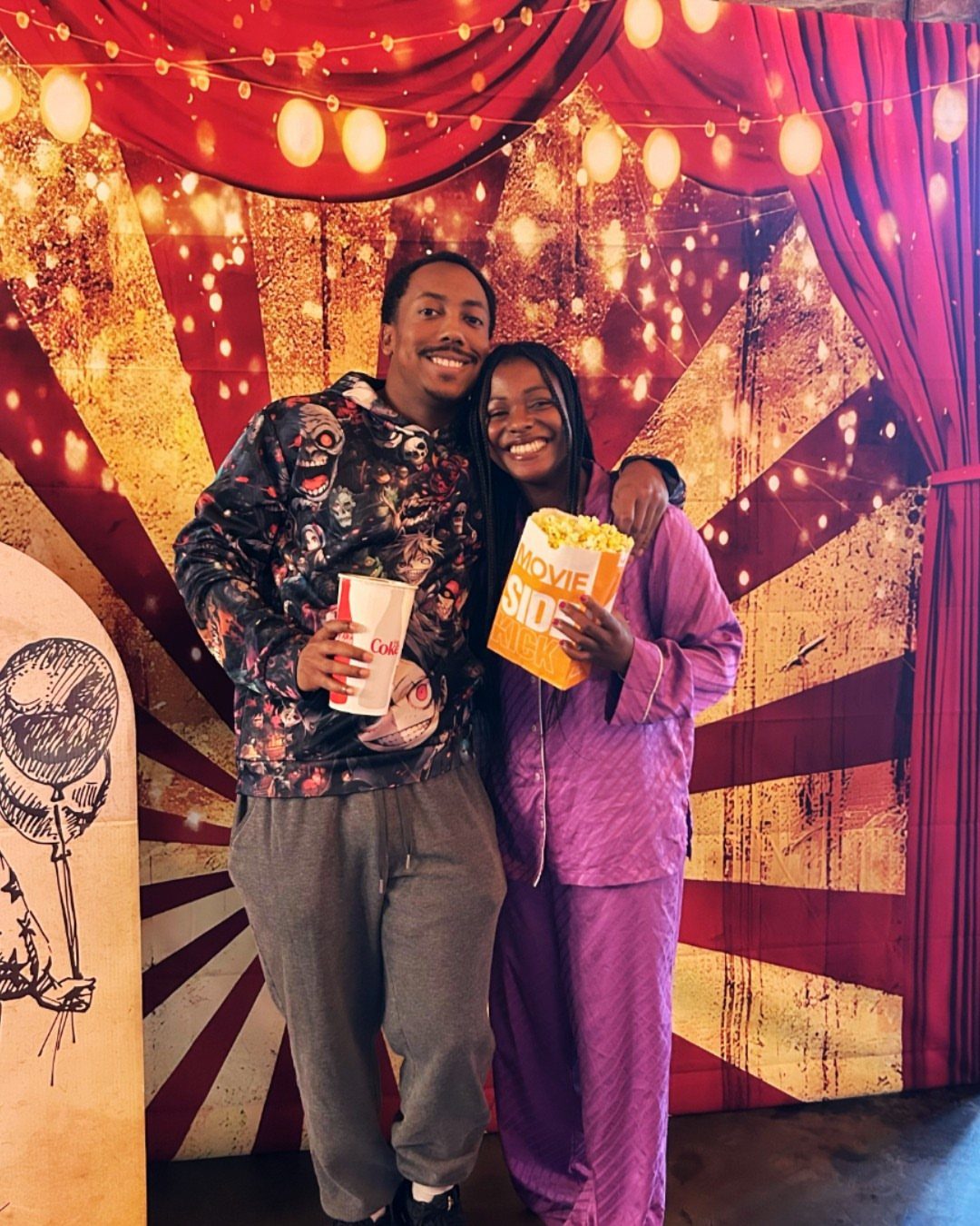 Man and woman in pajamas holding popcorn in front of a circus backdrop.