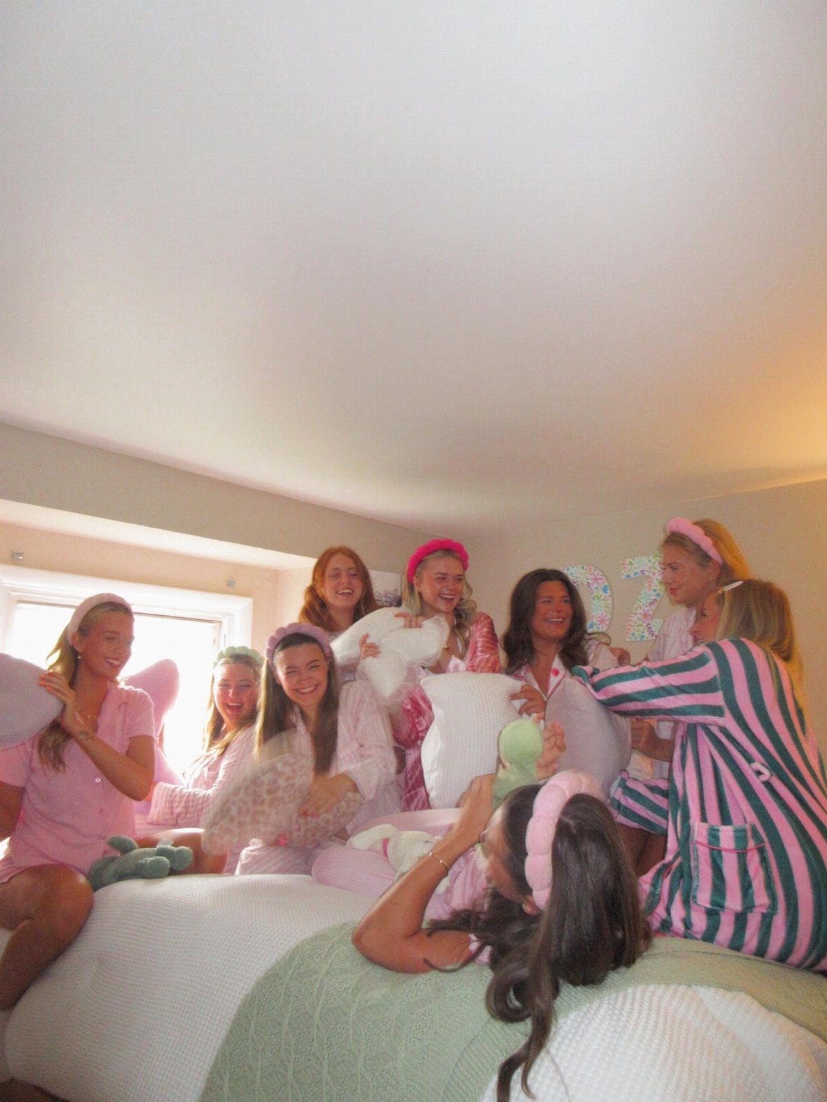 Young women in pink pajamas having a pillow fight on a large bed.