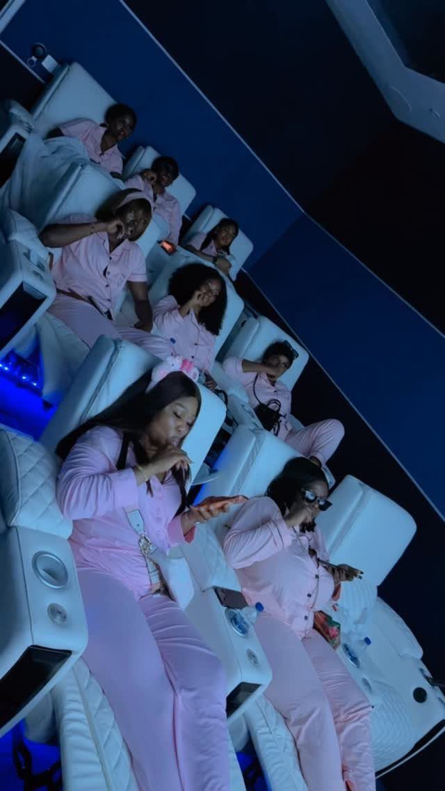 Women in pink pajamas sitting in white reclining cinema seats in a theater.