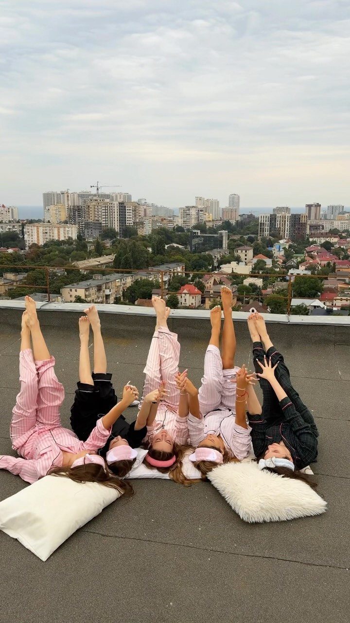 Six women in pajamas and sleep masks lying in a circle on a rooftop.