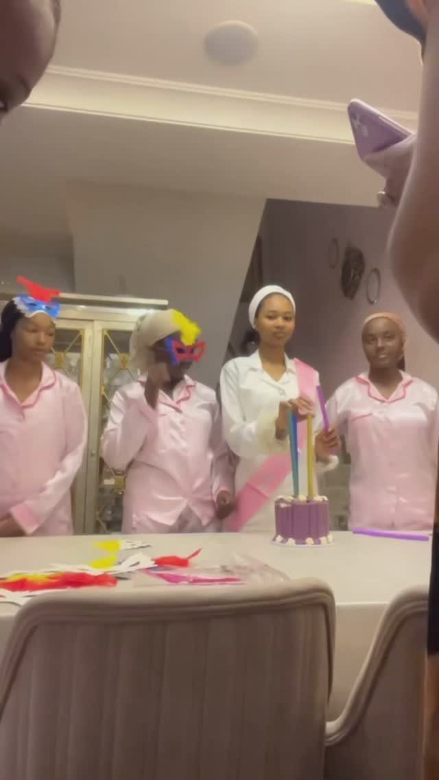 Four women wearing matching pink and white pajama sets gathered around a cake.
