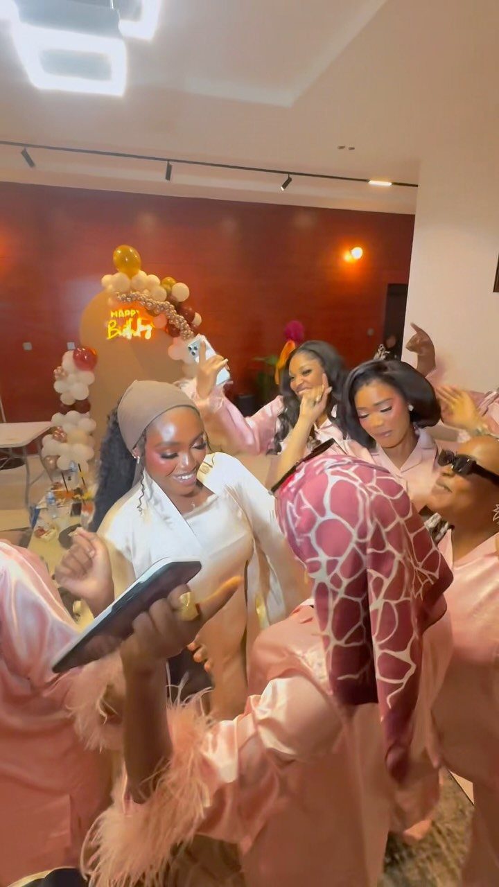 Women wearing pink and white satin robes and headwraps at a party.