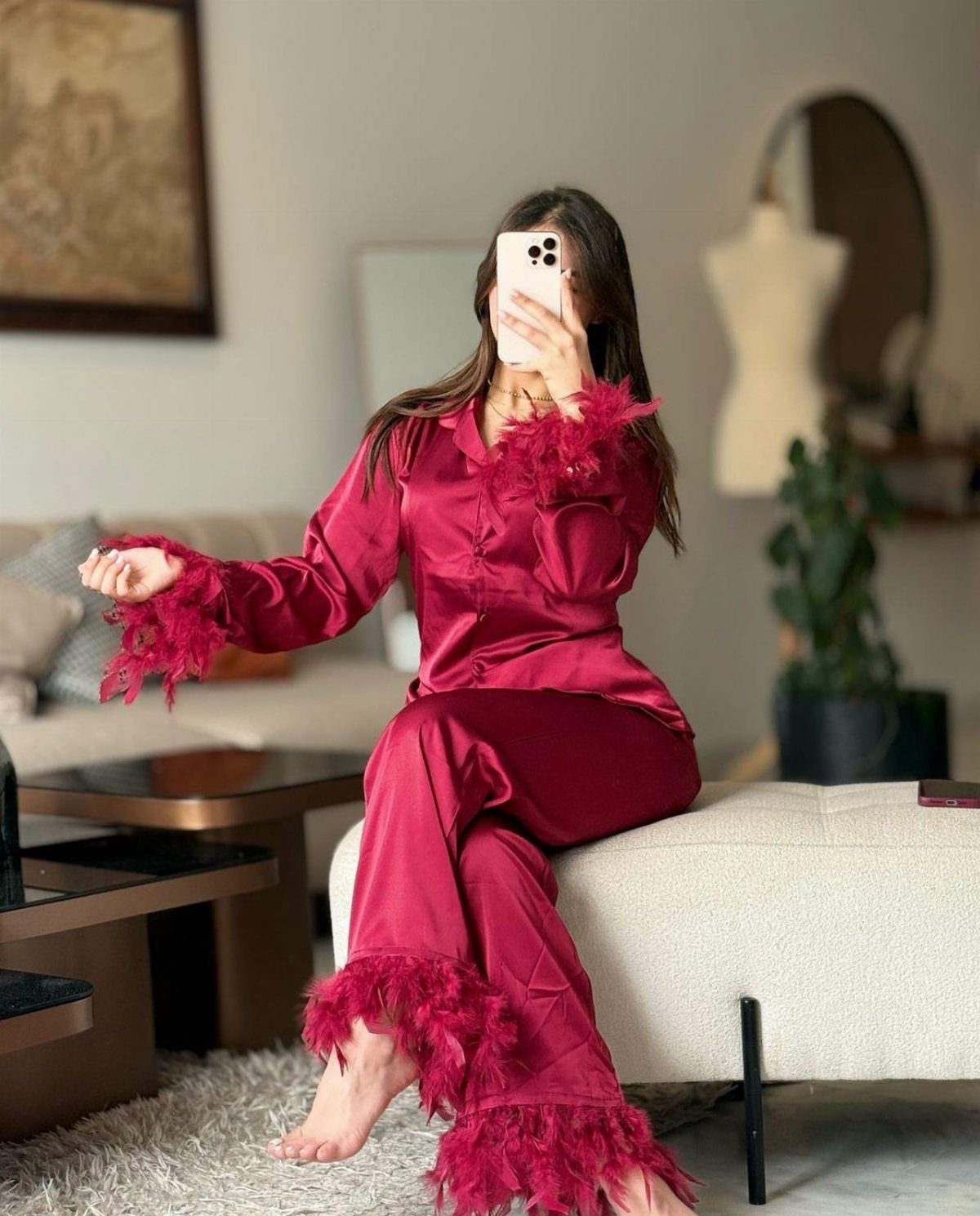 Woman wearing a red satin pajama set with feather trim taking a selfie.