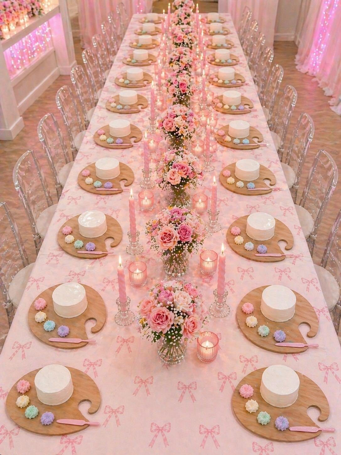 Long table set with artist palette plates, small cakes, and pink floral centerpieces.
