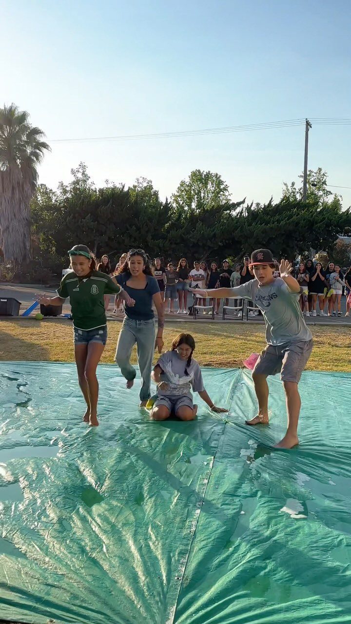Teenagers playing a game on a large green tarp in an outdoor setting.