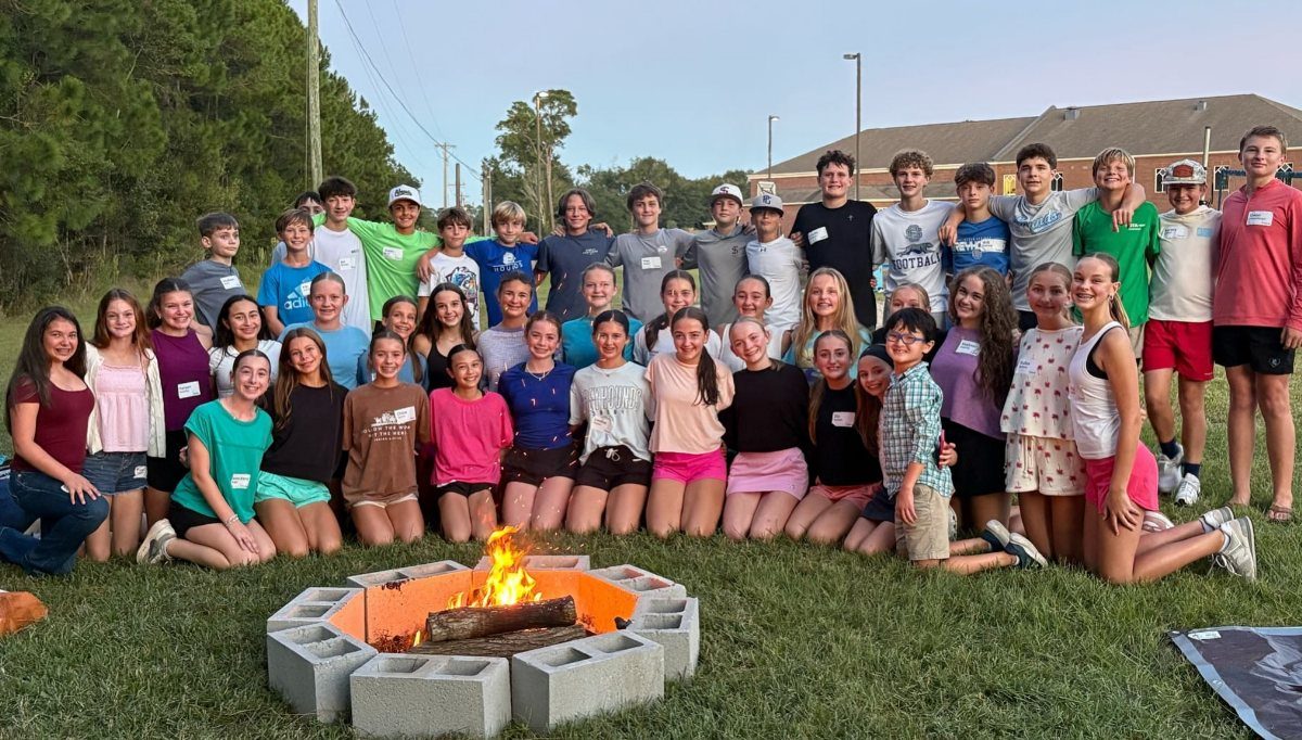 Teenagers posing in a circle around a lit bonfire in a grassy field.