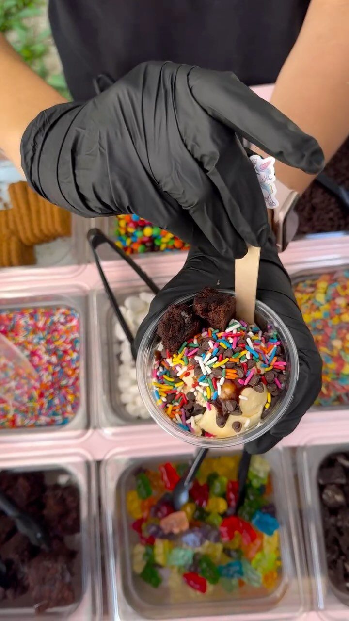 Ice cream sundae with toppings held over a variety of dessert bar ingredients.