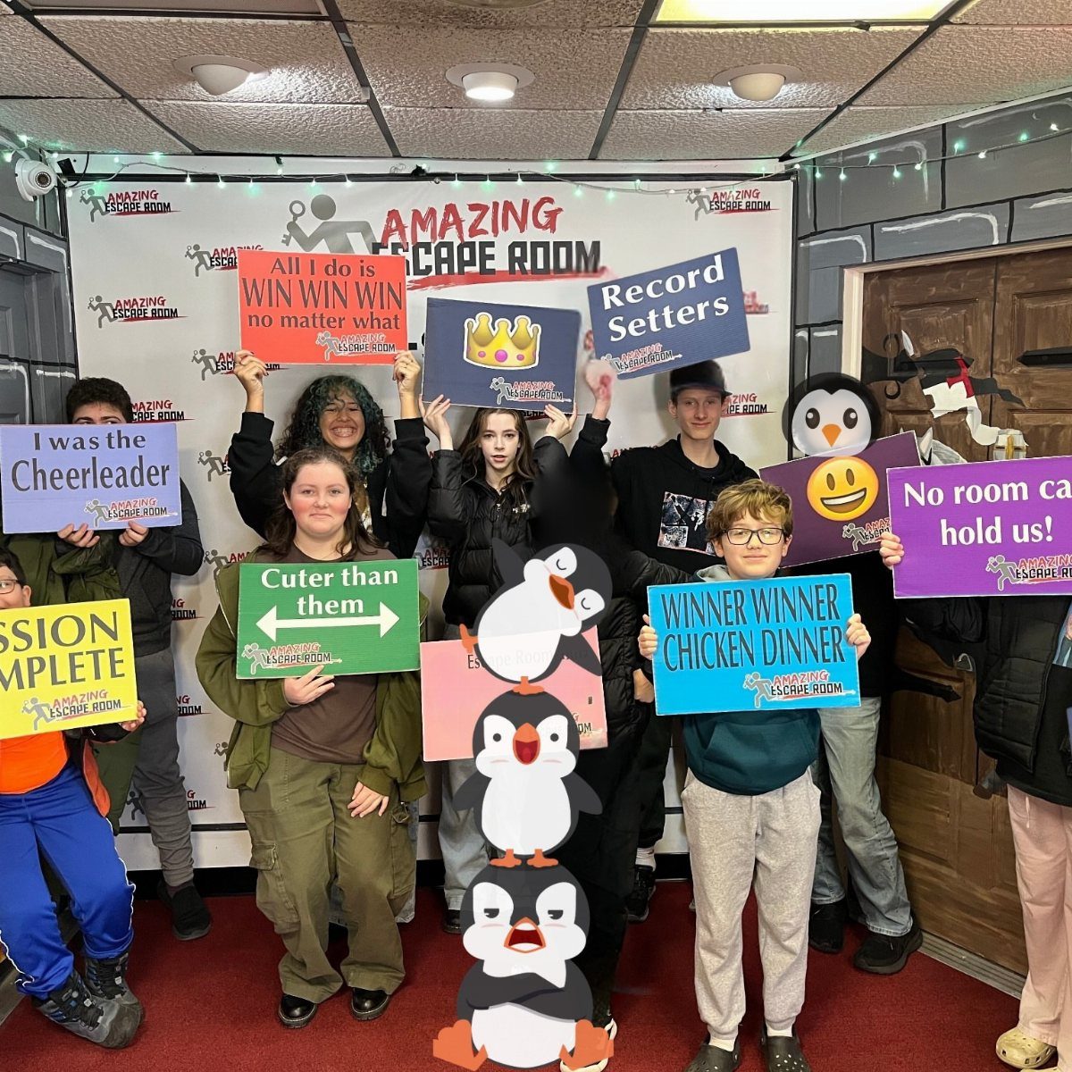 Teenagers posing with funny signs in front of an Amazing Escape Room backdrop.