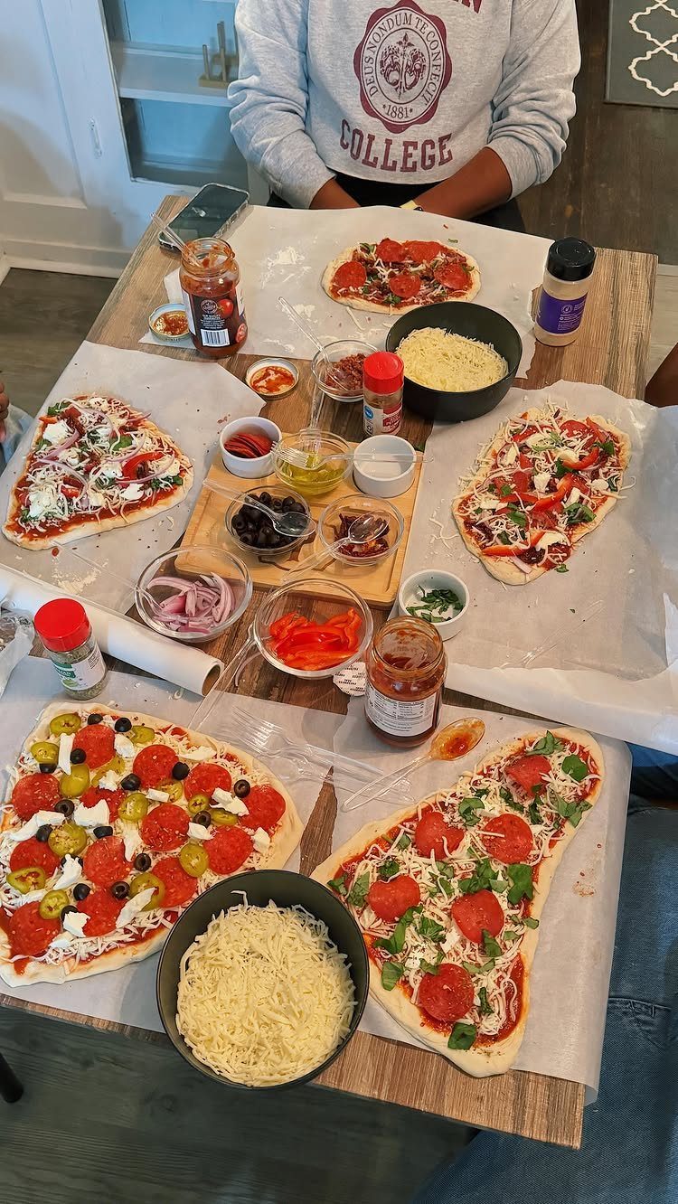 Homemade pizzas with various toppings and bowls of ingredients on a wooden table.