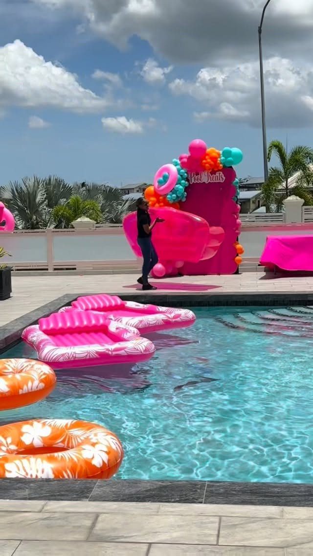 Swimming pool with colorful inflatable floats and a pink balloon party backdrop.