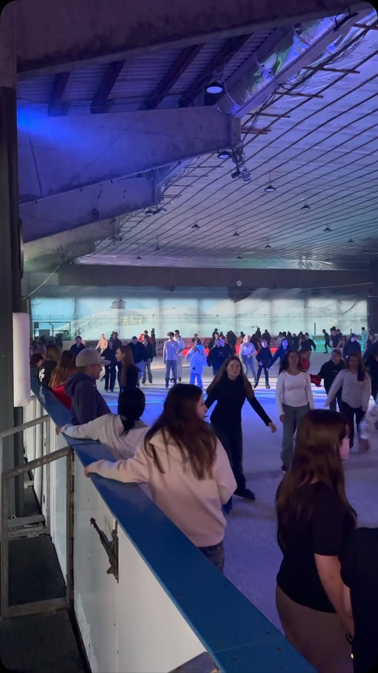 Teenagers ice skating at an indoor rink with blue lighting and railings.