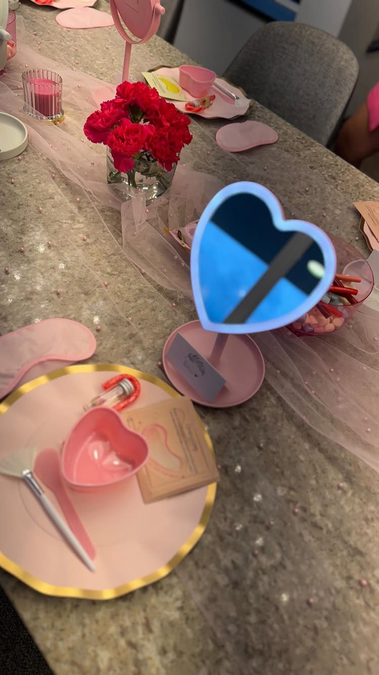 Spa party table setup with pink sleep masks, heart mirrors, and skincare products.