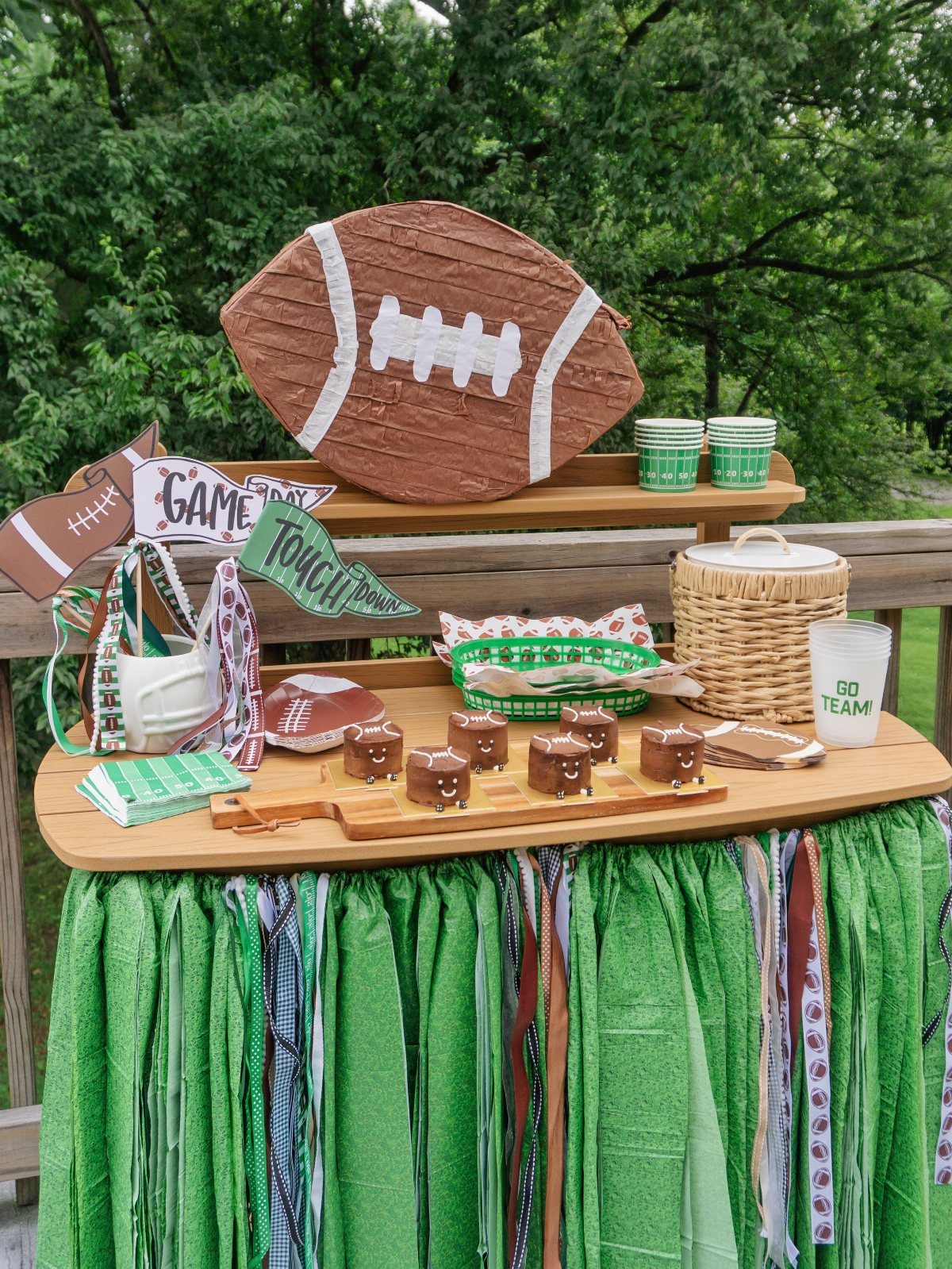 Sports-themed party table with football decorations, green accents, and football-shaped treats outdoors.