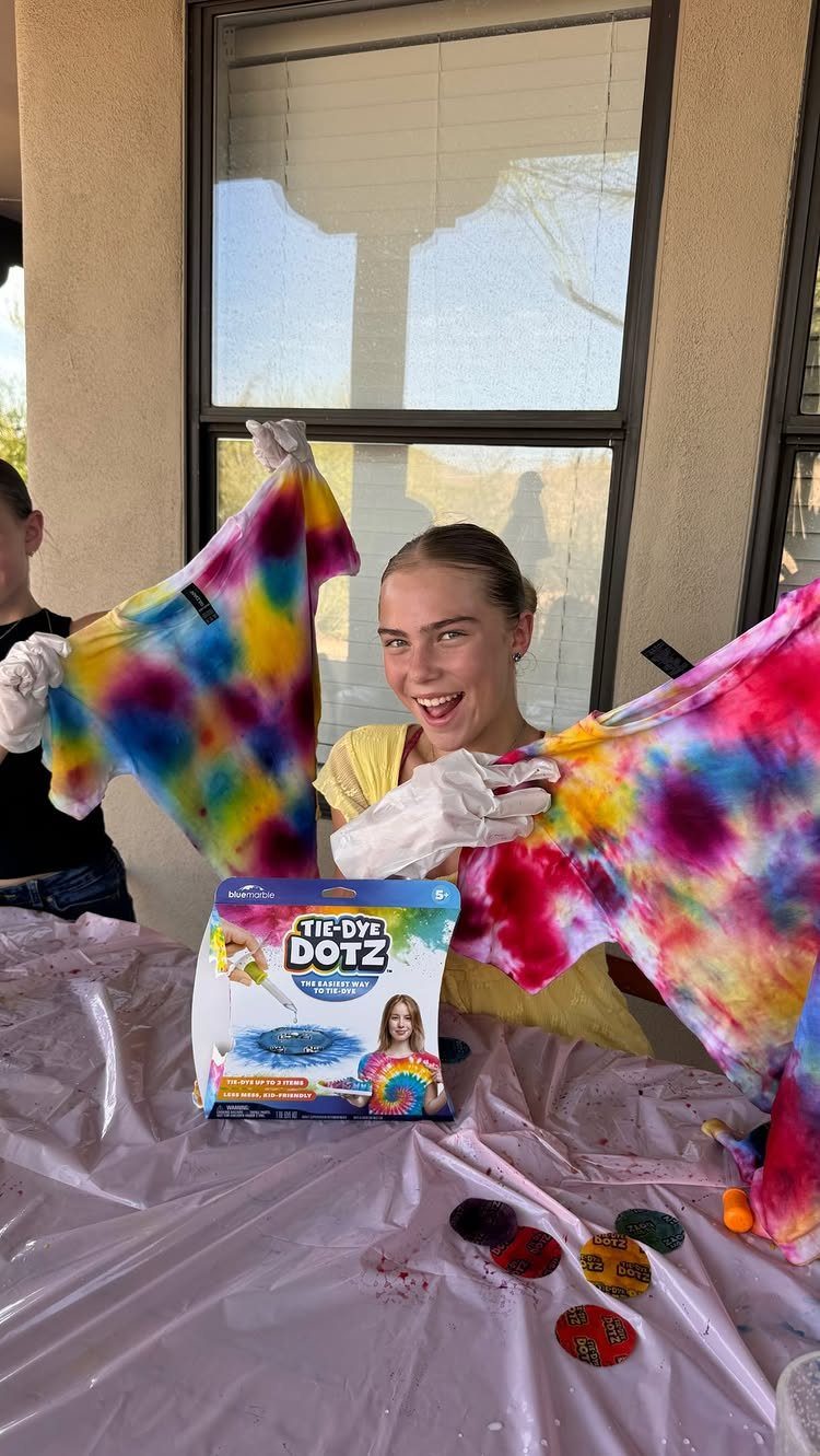 Teenage girl holding up colorful tie-dye t-shirts next to a tie-dye kit.