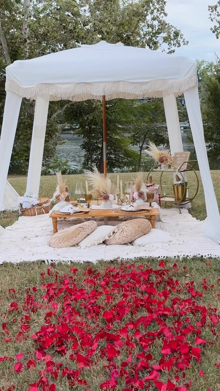 White canopy tent with low wooden table and pillows by a scenic lake
