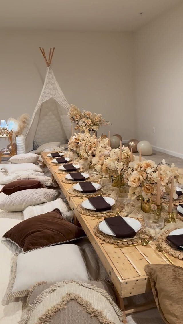 Low wooden table with floral centerpieces and floor pillows inside a room with teepee.