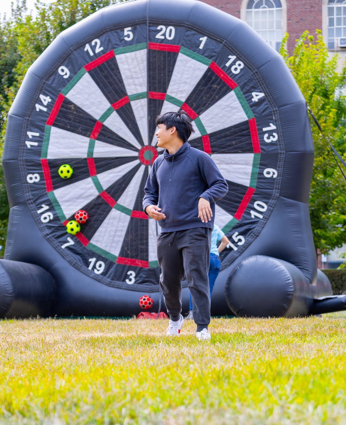 Man standing in front of a giant inflatable dartboard on a grassy lawn