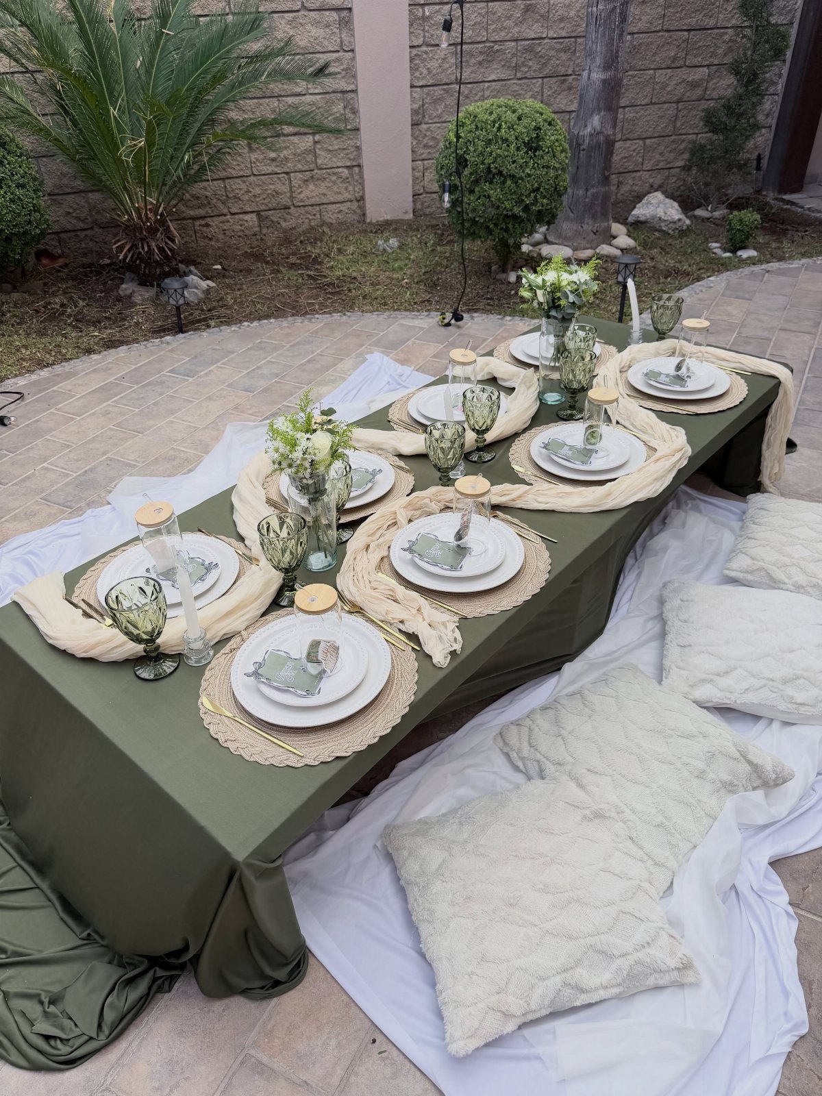 Low picnic table with olive green cloth, white plates, and white floor pillows.