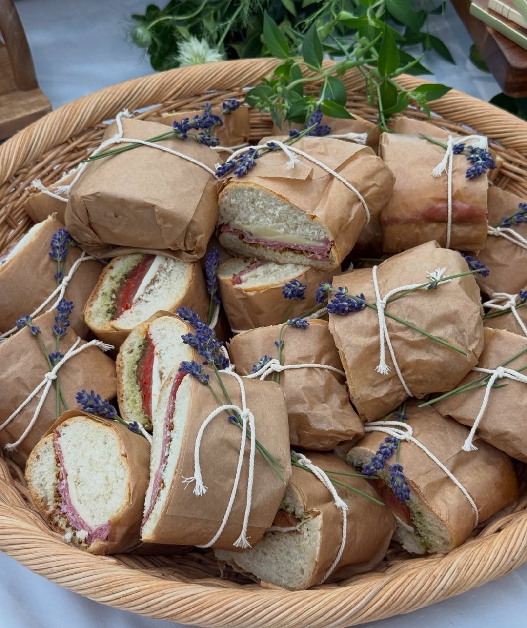 Sandwiches wrapped in brown paper and lavender tied with string in a wicker basket