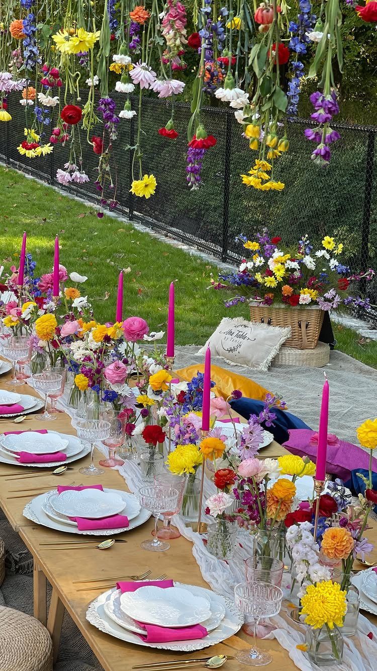 Wooden outdoor party table decorated with colorful fresh flower centerpieces and hanging blooms.