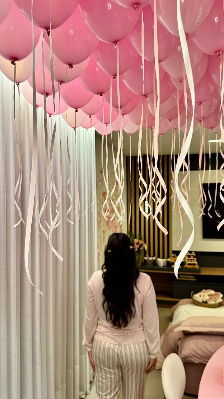 Woman standing under a ceiling filled with pink balloons and hanging white ribbons.