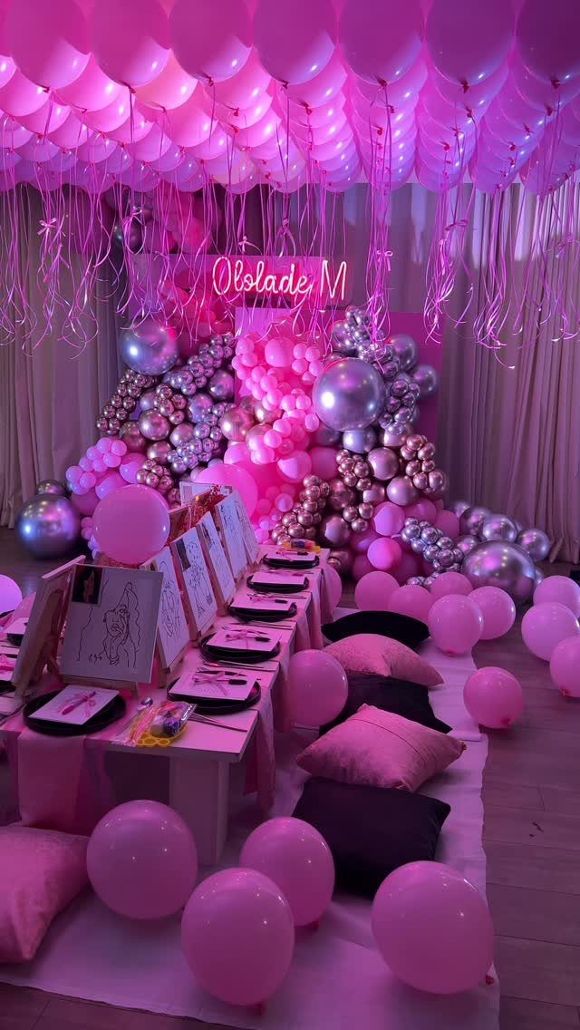 Pink and silver balloon decorations with floor pillows and low tables for a party.