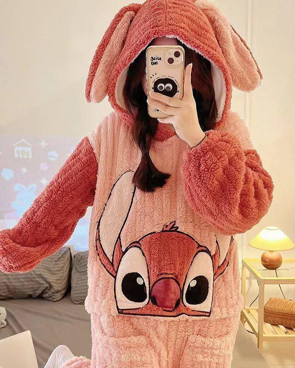 Person wearing a pink plush Stitch animal onesie taking a mirror selfie in bedroom