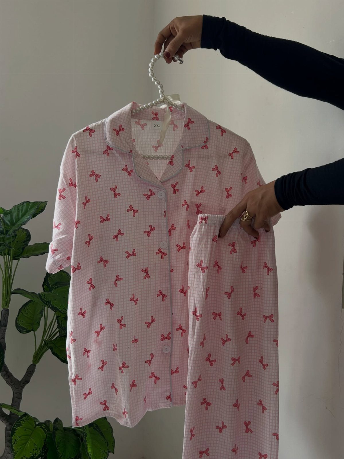 Pink and white checkered pajama set with red bows held by hands.