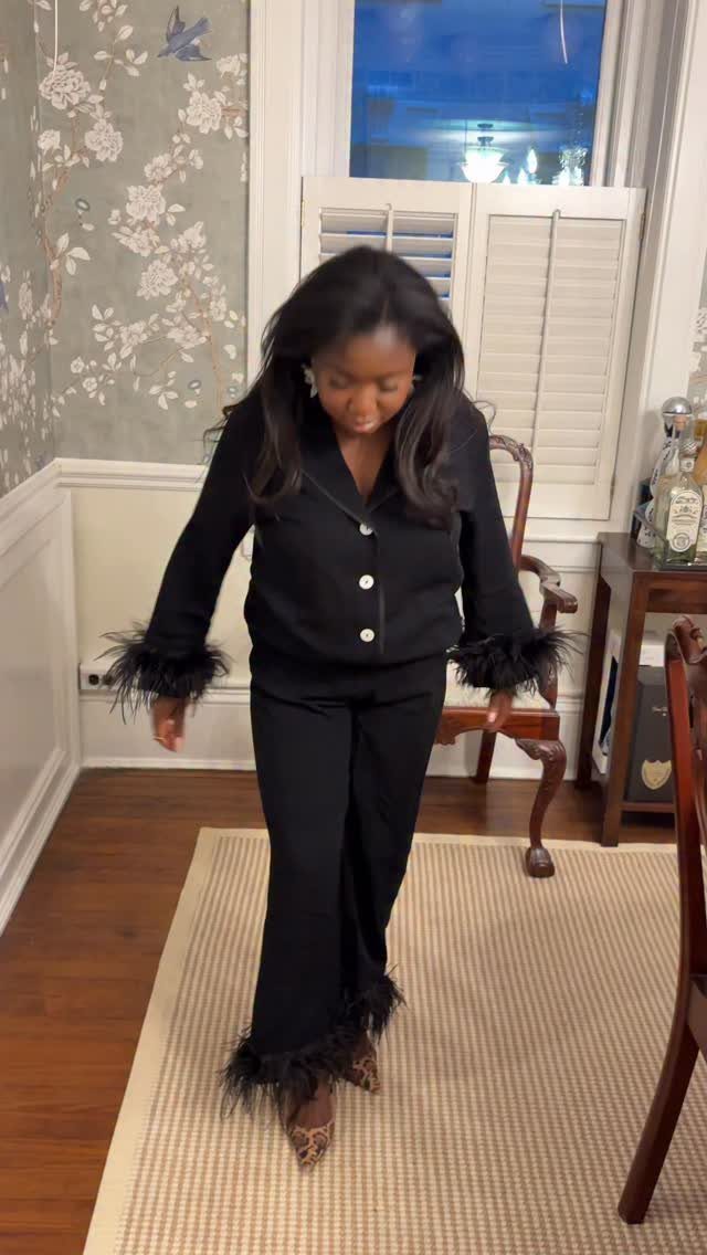 Woman wearing black luxury pajama set with feather trim on cuffs and hems.
