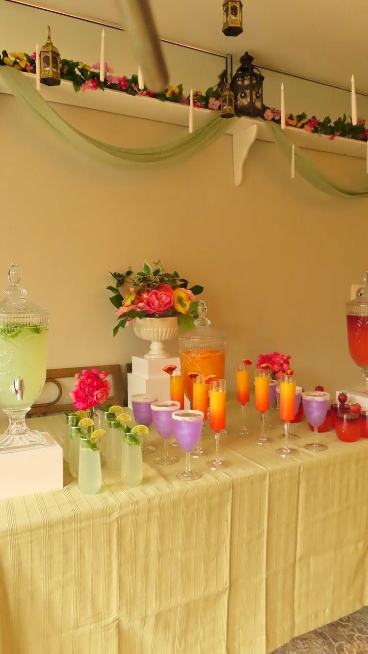 Colorful drink station with various beverages and flowers on a yellow tablecloth.