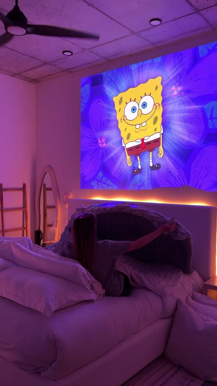 Person in bed watching a SpongeBob SquarePants projection in a purple-lit room