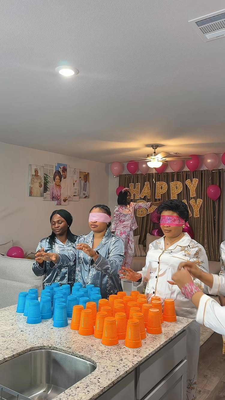 Women in pajamas playing a blindfolded game with colorful plastic cups at a party.