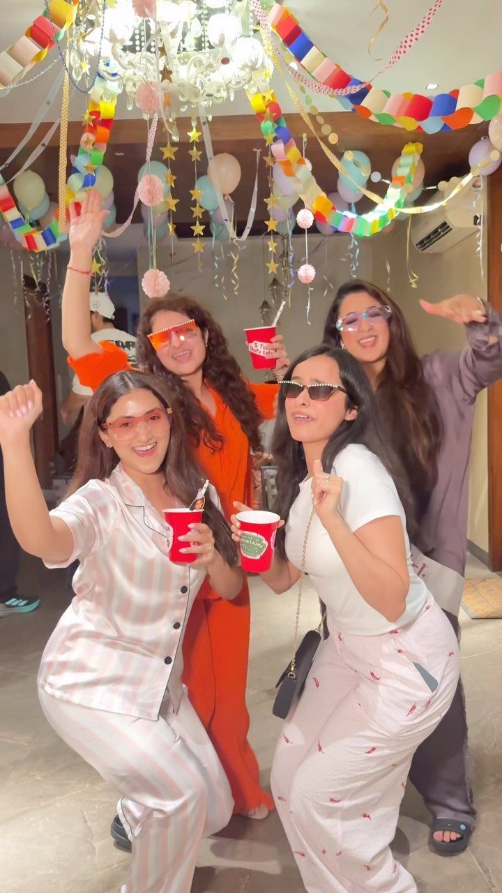 Four friends in pajamas and sunglasses posing at a decorated pajama party.