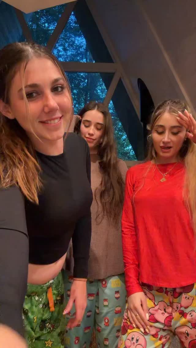 Three young women wearing colorful patterned pajama pants and long-sleeved shirts posing together.