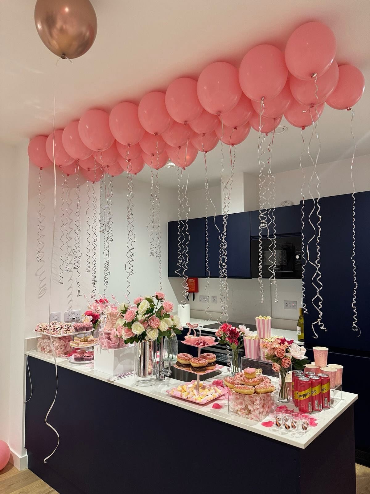 Pink balloons and desserts on a kitchen counter for a themed party celebration.